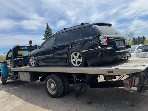 Collision-damaged Subaru wagon loaded on a Forest City Roadside flatbed tow truck